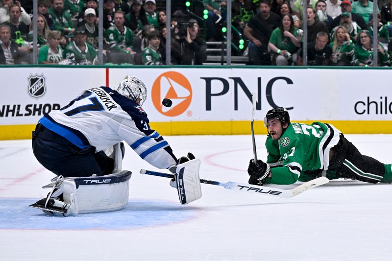 May 11, 2025; Dallas, Texas, USA; Dallas Stars left wing Mason Marchment (27) is tripped up as he shoots the puck towards Winnipeg Jets goaltender Connor Hellebuyck (37) during the second period in game three of the second round of the 2025 Stanley Cup Playoffs at American Airlines Center. Mandatory Credit: Jerome Miron-Imagn Images