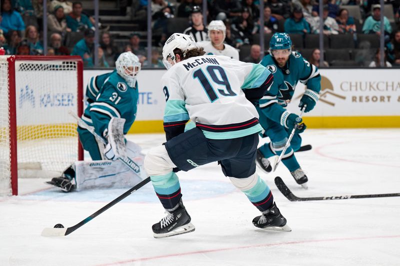 Apr 5, 2025; San Jose, California, USA; Seattle Kraken left wing Jared McCann (19) shoots the puck against San Jose Sharks goaltender Georgi Romanov (31) and defenseman Timothy Liljegren (37) during the third period at SAP Center at San Jose. Mandatory Credit: Robert Edwards-Imagn Images