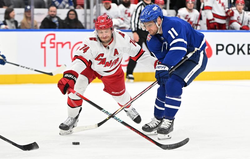 Dec 30, 2023; Toronto, Ontario, CAN; Carolina Hurricanes defenseman Jaccob Slavin (74) knocks the puck away from Toronto Maple Leafs forward Max Domi (11) in the first period at Scotiabank Arena. Mandatory Credit: Dan Hamilton-USA TODAY Sports