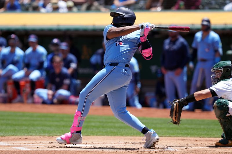 Jun 9, 2024; Oakland, California, USA; Toronto Blue Jays first baseman Vladimir Guerrero Jr. (27) hits a single against the Oakland Athletics during the first inning at Oakland-Alameda County Coliseum. Mandatory Credit: Darren Yamashita-USA TODAY Sports