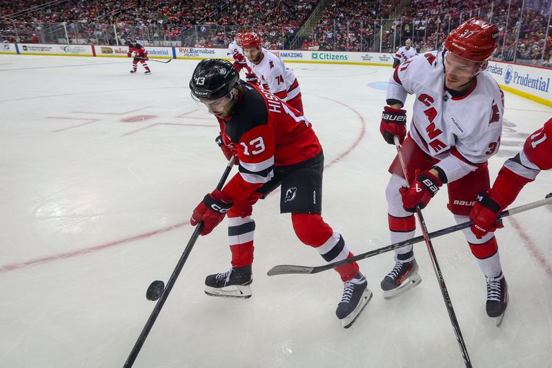 Nov 21, 2024; Newark, New Jersey, USA; New Jersey Devils center Nico Hischier (13) and Carolina Hurricanes right wing Andrei Svechnikov (37) battle for the puck during the second period at Prudential Center. Mandatory Credit: Ed Mulholland-Imagn Images