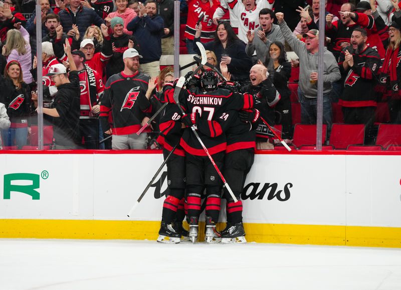 Nov 25, 2024; Raleigh, North Carolina, USA;  Carolina Hurricanes defenseman Shayne Gostisbehere (4) is congratulated by center Seth Jarvis (24) right wing Andrei Svechnikov (37) and center Martin Necas (88) after his goal against the Dallas Stars during the third period at Lenovo Center. Mandatory Credit: James Guillory-Imagn Images