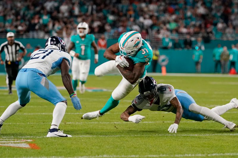 Tennessee Titans cornerback Sean Murphy-Bunting (0) attempts to bring down Miami Dolphins running back Raheem Mostert (31) during the first half of an NFL football game, Monday, Dec. 11, 2023, in Miami, Fla. (AP Photo/Lynne Sladky)