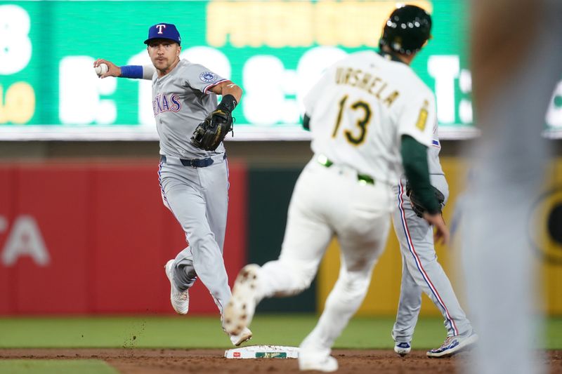 Apr 23, 2025; West Sacramento, California, USA; Texas Rangers shortstop Nick Ahmed (23) turns a double play in front of Athletics third baseman Gio Urshela (13) in the third inning at Sutter Health Park. Mandatory Credit: Cary Edmondson-Imagn Images