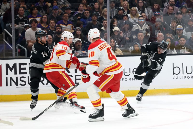 Dec 13, 2025; Los Angeles, California, USA;  Los Angeles Kings center Anze Kopitar (11) shoots the puck between Calgary Flames left wing Jonathan Huberdeau (10) and defenseman Hunter Brzustewicz (48) during the second period at Crypto.com Arena. Mandatory Credit: Kiyoshi Mio-Imagn Images