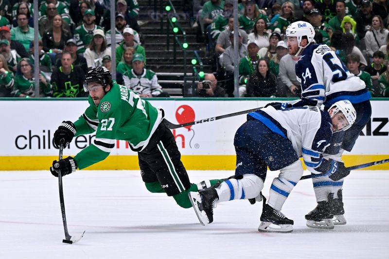May 11, 2025; Dallas, Texas, USA; Dallas Stars left wing Mason Marchment (27) is tripped up as he shoots the puck past Winnipeg Jets defenseman Neal Pionk (4) and defenseman Dylan Samberg (54) during the second period in game three of the second round of the 2025 Stanley Cup Playoffs at American Airlines Center. Mandatory Credit: Jerome Miron-Imagn Images