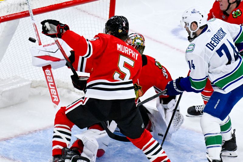 Oct 17, 2025; Chicago, Illinois, USA;  Vancouver Canucks left wing Jake Debrusk (74) scores past Chicago Blackhawks goaltender Spencer Knight (30) and  defenseman Connor Murphy (5) during the second period at the United Center. Mandatory Credit: Matt Marton-Imagn Images