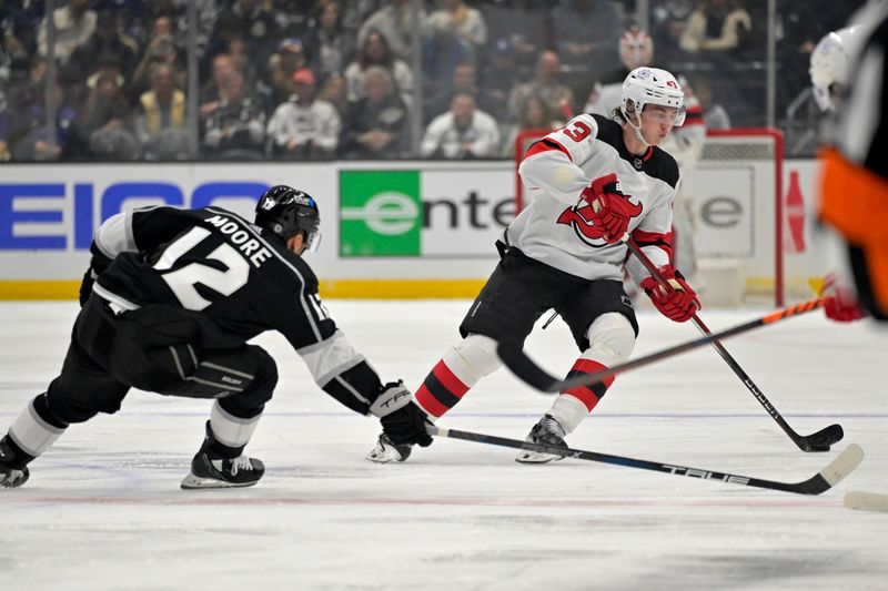 Mar 3, 2024; Los Angeles, California, USA; Los Angeles Kings left wing Trevor Moore (12) reaches in for the puck on New Jersey Devils defenseman Luke Hughes (43) in the first period at Crypto.com Arena. Mandatory Credit: Jayne Kamin-Oncea-USA TODAY Sports