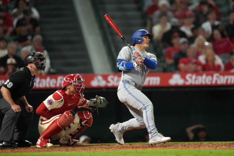 May 8, 2025; Anaheim, California, USA; Toronto Blue Jays center fielder Daulton Varsho (5) hits a RBI sacrifice fly in the sixth inning as Los Angeles Angels catcher Logan O'Hoppe (14) and home plate umpire Cory Blaser (89) watch at Angel Stadium. Mandatory Credit: Kirby Lee-Imagn Images