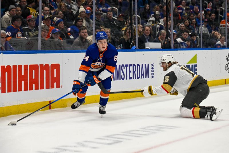Dec 9, 2025; Elmont, New York, USA; New York Islanders center Calum Ritchie (64) controls the puck defended by Vegas Golden Knights defenseman Noah Hanifin (15)  during the second period at UBS Arena. Mandatory Credit: Dennis Schneidler-Imagn Images