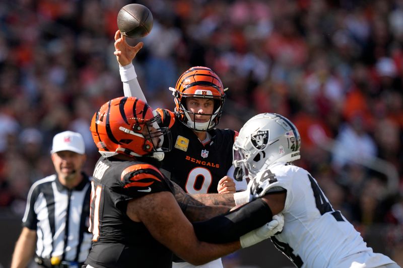 Cincinnati Bengals quarterback Joe Burrow, middle, passes as guard Cody Ford, left, blocks Las Vegas Raiders defensive end K'Lavon Chaisson during the first half of an NFL football game in Cincinnati, Sunday, Nov. 3, 2024. (AP Photo/Carolyn Kaster)