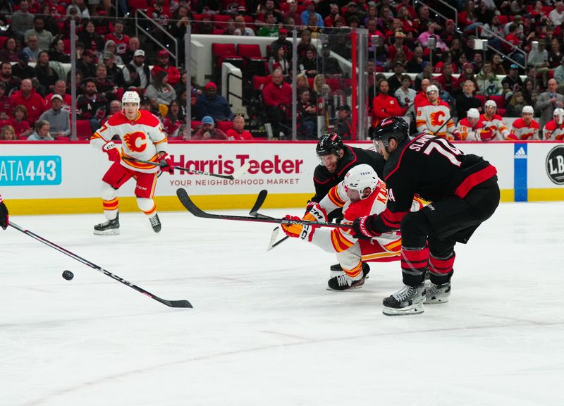 Mar 10, 2024; Raleigh, North Carolina, USA;  Calgary Flames center Nazem Kadri (91) gets the shot away between Carolina Hurricanes center Jordan Staal (11) and defenseman Jaccob Slavin (74) during the second period at PNC Arena. Mandatory Credit: James Guillory-USA TODAY Sports