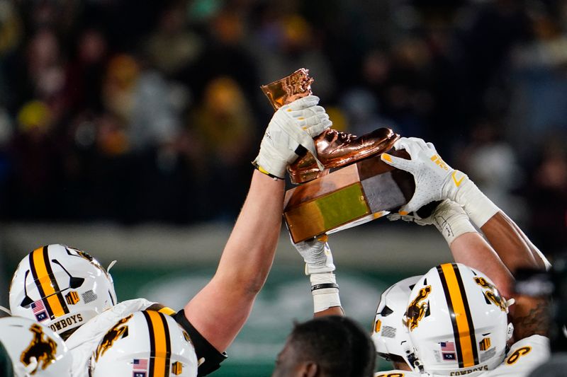 Nov 12, 2022; Fort Collins, Colorado, USA; Wyoming Cowboys players celebrate with the Bronze Boot trophy after defeating the Colorado State Rams 14-13 at Sonny Lubick Field at Canvas Stadium. Mandatory Credit: Michael Madrid-USA TODAY Sports