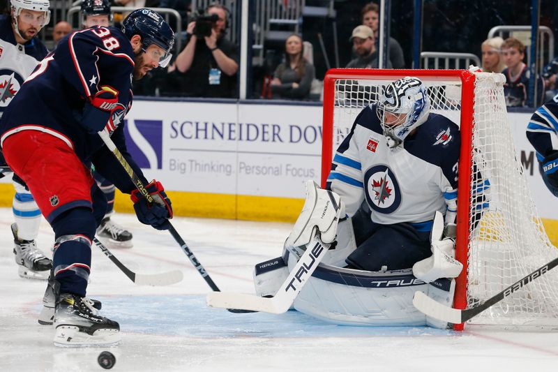 Mar 17, 2024; Columbus, Ohio, USA; The rebound of a Winnipeg Jets goalie Connor Hellebuyck (37) save deflects past Columbus Blue Jackets center Boone Jenner (38) during the second period at Nationwide Arena. Mandatory Credit: Russell LaBounty-USA TODAY Sports