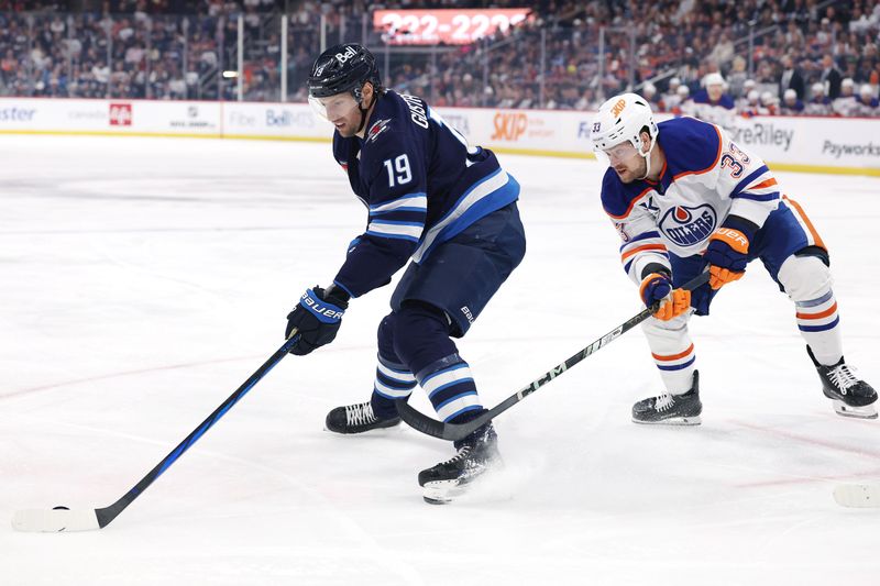 Apr 13, 2025; Winnipeg, Manitoba, CAN; Winnipeg Jets center David Gustafsson (19) is checked by Edmonton Oilers left wing Viktor Arvidsson (33) in the first period at Canada Life Centre. Mandatory Credit: James Carey Lauder-Imagn Images