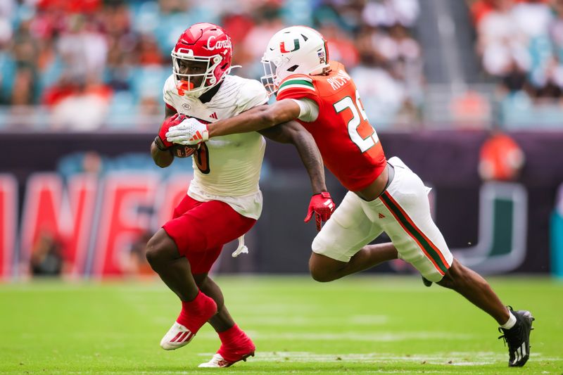 Nov 18, 2023; Miami Gardens, Florida, USA; Louisville Cardinals wide receiver Chris Bell (0) breaks a tackle attempt from Miami Hurricanes defensive back Jadais Richard (25) during the second quarter at Hard Rock Stadium. Mandatory Credit: Sam Navarro-USA TODAY Sports