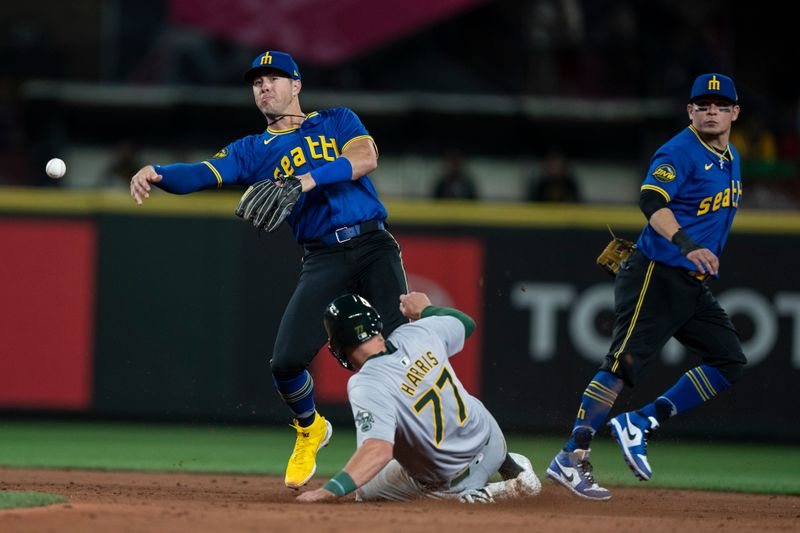 May 10, 2024; Seattle, Washington, USA; Seattle Mariners shortstop Dylan Moore (25) attempts to turn a double play after forcing out Oakland Athletics third baseman Brett Harris (77) at second base eighth inning at T-Mobile Park. At right is Seattle Mariners second baseman Josh Rojas (4). Mandatory Credit: Stephen Brashear-USA TODAY Sports