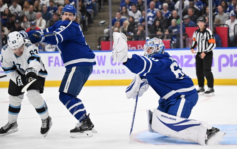 Nov 24, 2024; Toronto, Ontario, CAN;  Toronto Maple Leafs goalie Joseph Woll (60) reaches for the puck as defenseman Simon Benoit (2) fends off Utah Hockey Club forward Matias Maccelli (63) in the second period at Scotiabank Arena. Mandatory Credit: Dan Hamilton-Imagn Images