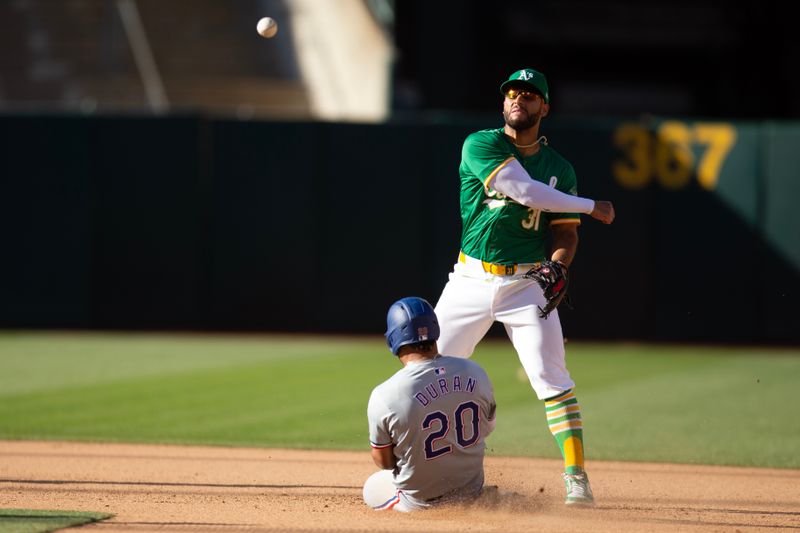 May 8, 2024; Oakland, California, USA; Oakland Athletics second baseman Abraham Toro (31) throws over Texas Rangers third baseman Ezequiel Duran (20) to complete a double play during the seventh inning at Oakland-Alameda County Coliseum. Mandatory Credit: D. Ross Cameron-USA TODAY Sports