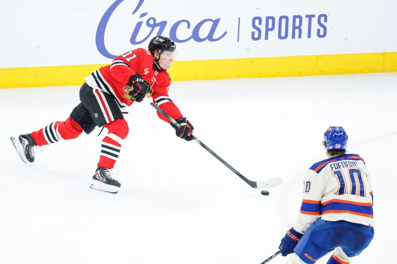 Jan 12, 2026; Chicago, Illinois, USA; Chicago Blackhawks center Oliver Moore (11) shoots against Edmonton Oilers center Trent Frederic (10) during the second period at United Center. Mandatory Credit: Kamil Krzaczynski-Imagn Images