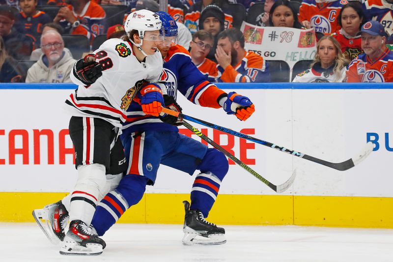 Oct 12, 2024; Edmonton, Alberta, CAN; Chicago Blackhawks forward Connor Bedard (98) and Edmonton Oilers defensemen Brett Kulak (27)  chase a loose puck during the second period at Rogers Place. Mandatory Credit: Perry Nelson-Imagn Images