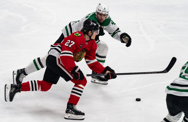 Apr 6, 2024; Chicago, Illinois, USA; Chicago Blackhawks left winger Lukas Reichel (27) pushes the puck past Dallas Stars defenseman Miro Heiskanen (4) during the second period at United Center. Mandatory Credit: Seeger Gray-USA TODAY Sports