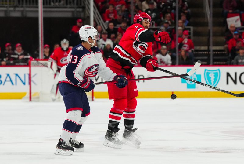 Nov 26, 2023; Raleigh, North Carolina, USA; Carolina Hurricanes defenseman Jalen Chatfield (5) knocked the puck out of the air away from Columbus Blue Jackets left wing Johnny Gaudreau (13) during the first period at PNC Arena. Mandatory Credit: James Guillory-USA TODAY Sports