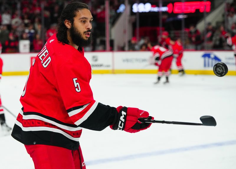 Dec 23, 2023; Raleigh, North Carolina, USA; Carolina Hurricanes defenseman Jalen Chatfield (5) bounces a puck on his stick before the game against the New York Islanders at PNC Arena. Mandatory Credit: James Guillory-USA TODAY Sports