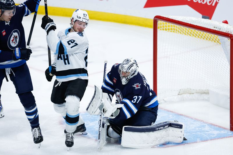 Nov 5, 2024; Winnipeg, Manitoba, CAN;  Winnipeg Jets goalie Connor Hellebuyck (37) makes a save as Utah Hockey Club forward Barrett Hayton (27) looks for a rebound during the third period at Canada Life Centre. Mandatory Credit: Terrence Lee-Imagn Images