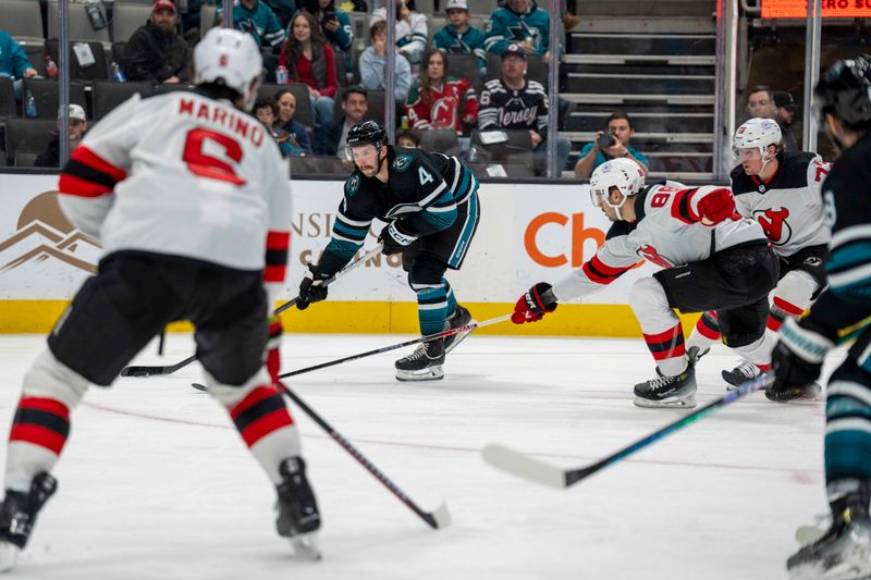 Feb 27, 2024; San Jose, California, USA;  San Jose Sharks defenseman Kyle Burroughs (4) shoots the puck against New Jersey Devils defenseman Kevin Bahl (88) during the second period at SAP Center at San Jose. Mandatory Credit: Neville E. Guard-USA TODAY Sports