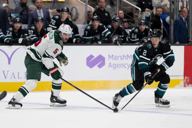 Nov 7, 2024; San Jose, California, USA;  Minnesota Wild defenseman Jake Middleton (5) and San Jose Sharks center Will Smith (2) reach for the puck during the first period at SAP Center at San Jose. Mandatory Credit: Stan Szeto-Imagn Images