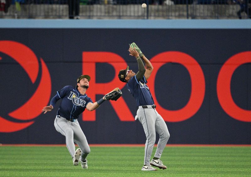 May 17, 2024; Toronto, Ontario, CAN;  Tampa Bay Rays center Jonny DeLuca (21) reaches up to catch a fly ball hit by Toronto Blue Jays catcher Danny Jansen (not shown) as right fielder Josh Lowe (15) backs up the play in the fifth inning at Rogers Centre. Mandatory Credit: Dan Hamilton-USA TODAY Sports