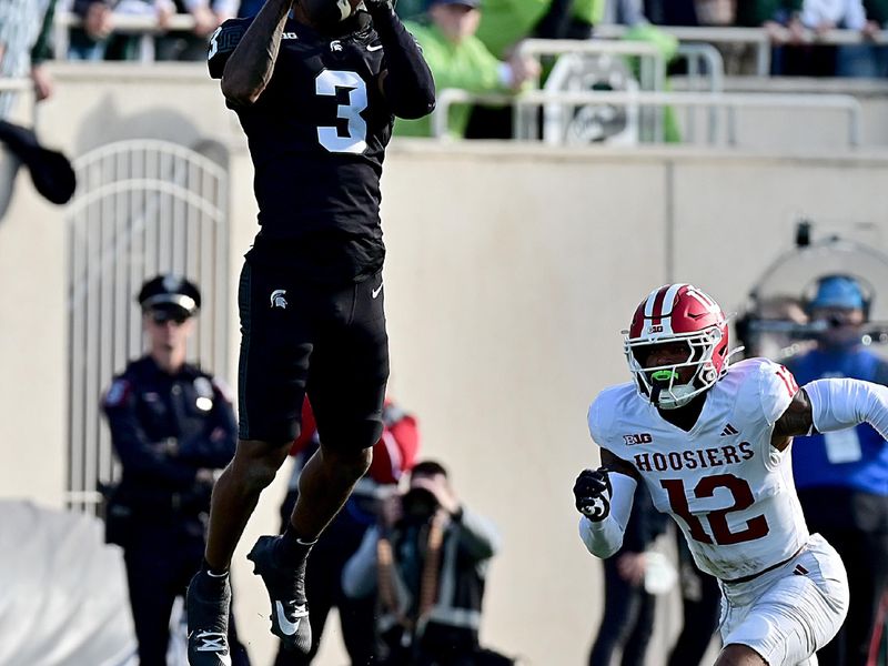 Nov 2, 2024; East Lansing, Michigan, USA;  Michigan State Spartans wide receiver Montorie Foster Jr. (3) goes way up in the air for a catch as Indiana Hoosiers defensive back Terry Jones Jr. (12) closes-in on him during the first quarter at Spartan Stadium. Mandatory Credit: Dale Young-Imagn Images