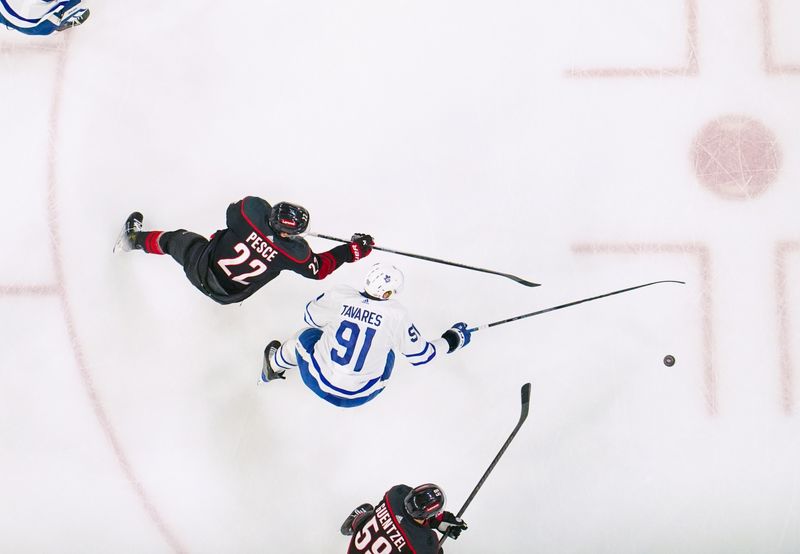 Mar 24, 2024; Raleigh, North Carolina, USA;  Carolina Hurricanes defenseman Brett Pesce (22) clears the puck away from Toronto Maple Leafs center John Tavares (91) during the first period at PNC Arena. Mandatory Credit: James Guillory-USA TODAY Sports