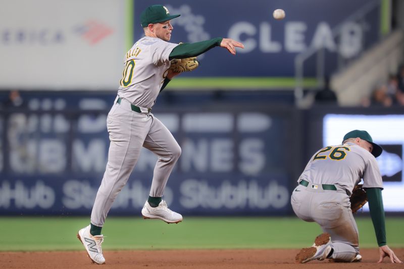 Apr 23, 2024; Bronx, New York, USA; Oakland Athletics shortstop Nick Allen (10) throws to first base for an out as third baseman Tyler Nevin (26) kneels during the second inning against the New York Yankees at Yankee Stadium. Mandatory Credit: Vincent Carchietta-USA TODAY Sports