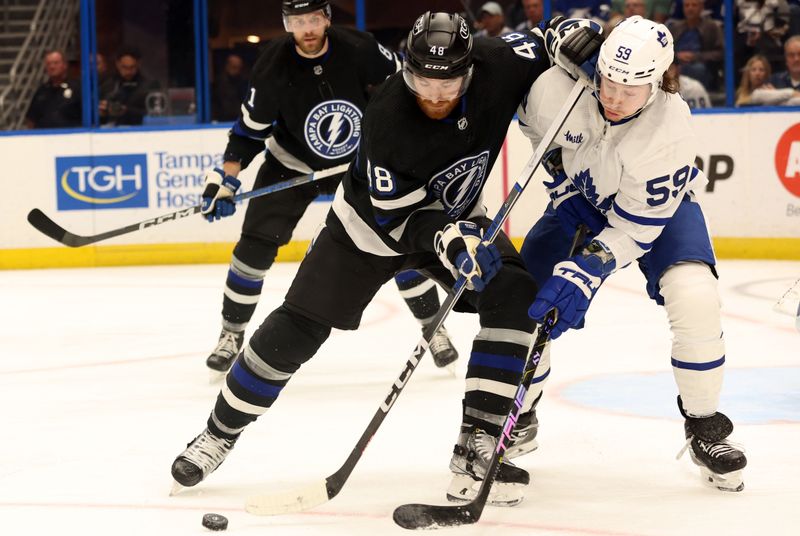 Apr 17, 2024; Tampa, Florida, USA; Tampa Bay Lightning defenseman Nick Perbix (48) and Toronto Maple Leafs left wing Tyler Bertuzzi (59) fight for a loose puck during the second period at Amalie Arena. Mandatory Credit: Kim Klement Neitzel-USA TODAY Sports