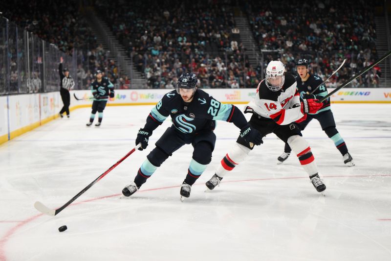 Jan 6, 2025; Seattle, Washington, USA; Seattle Kraken defenseman Joshua Mahura (28) plays the puck while defended by New Jersey Devils right wing Nathan Bastian (14) during the second period at Climate Pledge Arena. Mandatory Credit: Steven Bisig-Imagn Images