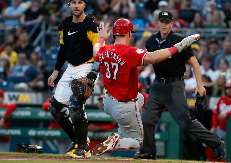 Aug 23, 2024; Pittsburgh, Pennsylvania, USA;  Cincinnati Reds catcher Tyler Stephenson (37) crosses home plate to score a run as Pittsburgh Pirates catcher Joey Bart (14) looks on during the fourth inning at PNC Park. Mandatory Credit: Charles LeClaire-USA TODAY Sports