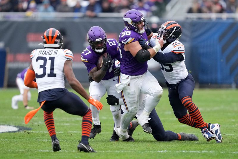 Minnesota Vikings running back Cam Akers (27) runs behind a block from center Garrett Bradbury (56) during the second half of an NFL football game Chicago Bears, Sunday, Nov. 24, 2024, in Chicago. (AP Photo/Charles Rex Arbogast)