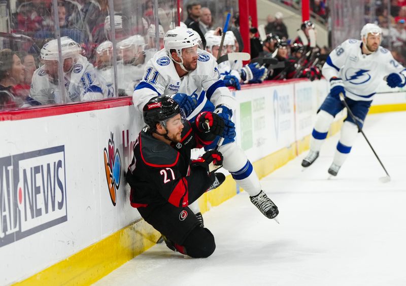 Mar 11, 2025; Raleigh, North Carolina, USA;  Tampa Bay Lightning center Luke Glendening (11) checks Carolina Hurricanes center Tyson Jost (27) during the first period at Lenovo Center. Mandatory Credit: James Guillory-Imagn Images