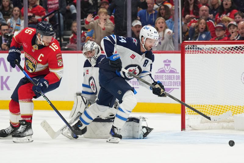 Nov 16, 2024; Sunrise, Florida, USA;  Winnipeg Jets defenseman Josh Morrissey (44) clears the puck out of the zone as Florida Panthers center Aleksander Barkov (16) follows on the play during the second period at Amerant Bank Arena. Mandatory Credit: Jim Rassol-Imagn Images