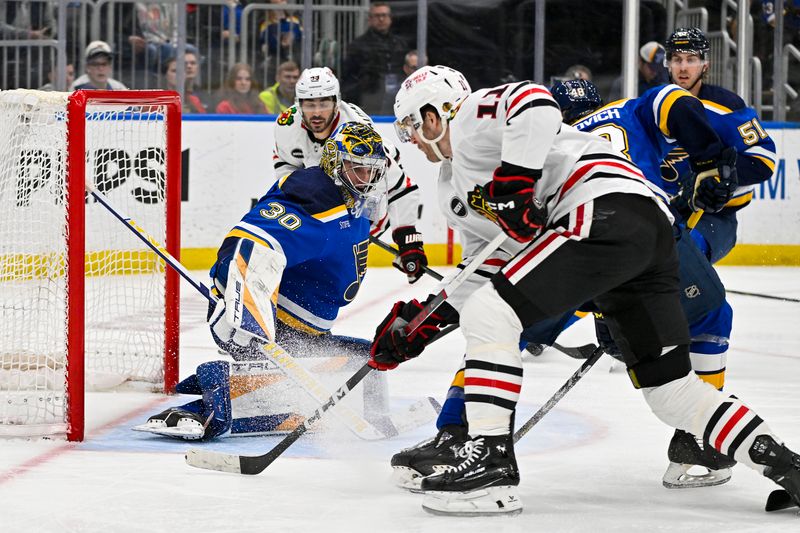 Apr 10, 2024; St. Louis, Missouri, USA;  St. Louis Blues goaltender Joel Hofer (30) defends the net against Chicago Blackhawks right wing Taylor Raddysh (11) during the third period at Enterprise Center. Mandatory Credit: Jeff Curry-USA TODAY Sports