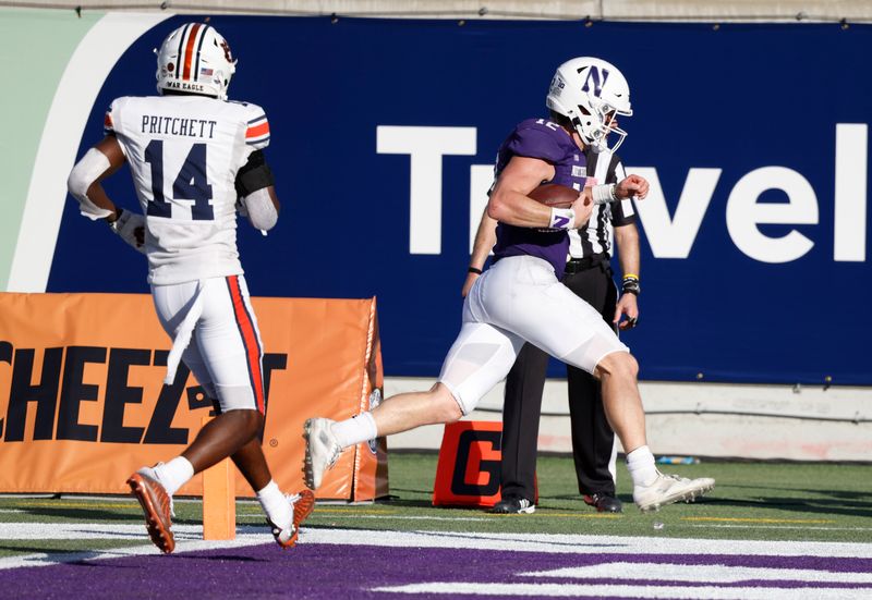 Jan 1, 2021; Orlando, FL, USA; Northwestern Wildcats quarterback Peyton Ramsey (12) runs in for the score ahead of Auburn Tigers defensive back Nehemiah Pritchett (14) during the second half at Camping World Stadium. Mandatory Credit: Reinhold Matay-USA TODAY Sports