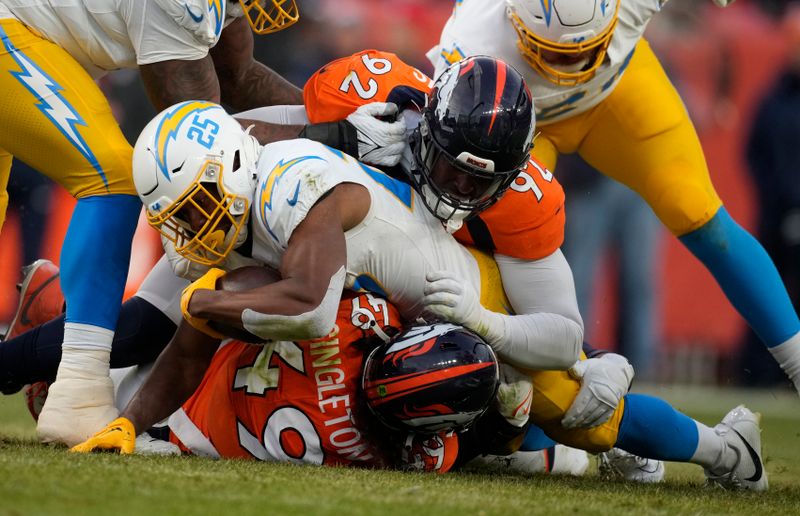 Los Angeles Chargers running back Joshua Kelley (25) is stopped by Denver Broncos defensive tackle Jonathan Harris (92) and Denver Broncos linebacker Alex Singleton (49) in the second half of an NFL football game in Empower Field at Mile High Sunday, Dec. 31, 2023, in Denver. (AP Photo/David Zalubowski)