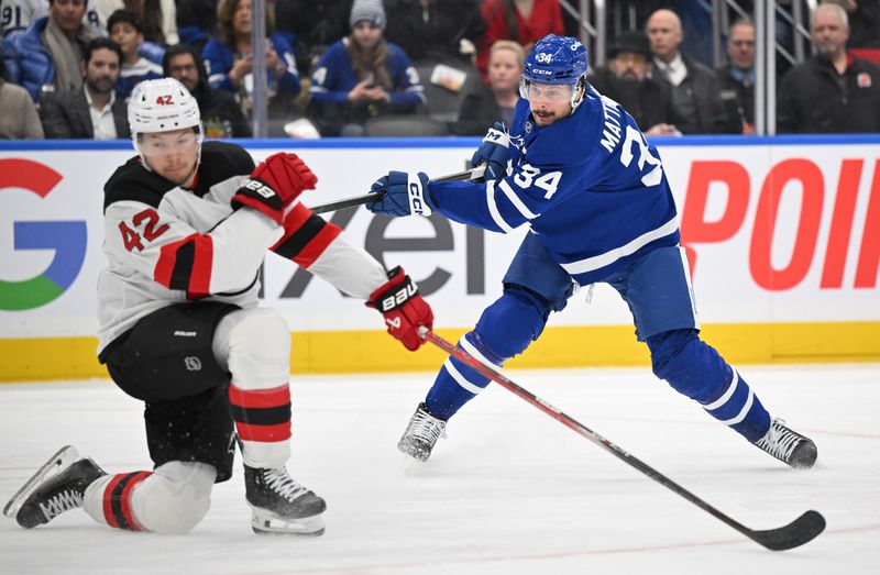 Jan 16, 2025; Toronto, Ontario, CAN; Toronto Maple Leafs forward Auston Matthews (34) shoots the puck past New Jersey Devils forward Curtis Lazar (42) in the first period at Scotiabank Arena. Mandatory Credit: Dan Hamilton-Imagn Images