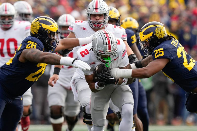 Nov 25, 2023; Ann Arbor, Michigan, USA; Michigan Wolverines defensive lineman Rayshaun Benny (26) and linebacker Junior Colson (25) tackle Ohio State Buckeyes wide receiver Emeka Egbuka (2) during the first half of the NCAA football game at Michigan Stadium. Mandatory Credit: Adam Cairns-USA TODAY Sports