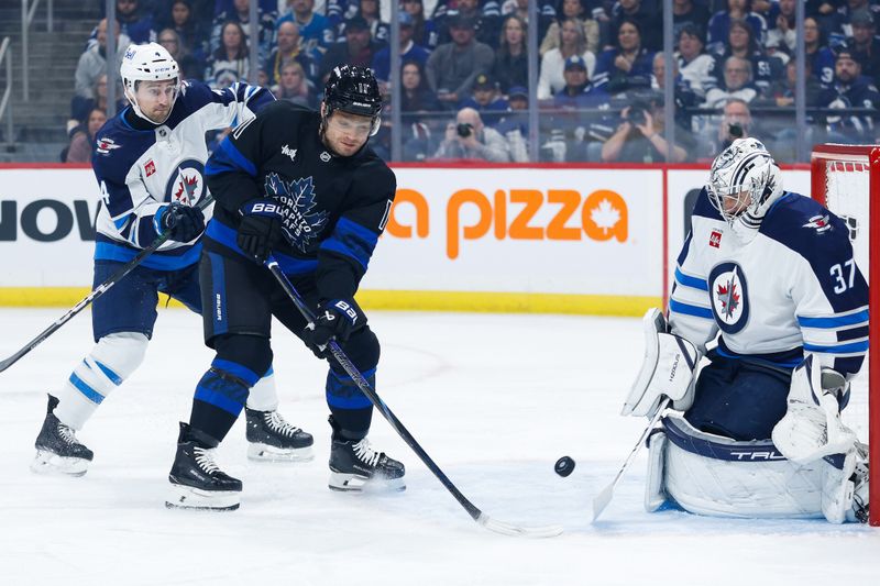 Oct 28, 2024; Winnipeg, Manitoba, CAN; Toronto Maple Leafs forward Max Domi (11) looks for a rebound from Winnipeg Jets goalie Connor Hellebuyck (37) during the first period at Canada Life Centre. Mandatory Credit: Terrence Lee-Imagn Images