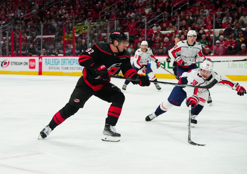 Apr 5, 2024; Raleigh, North Carolina, USA; Carolina Hurricanes center Evgeny Kuznetsov (92) gets the shot away past Washington Capitals defenseman Rasmus Sandin (38) during the first period at PNC Arena. Mandatory Credit: James Guillory-USA TODAY Sports