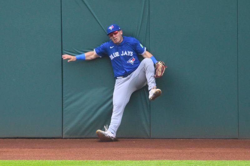 Jun 22, 2024; Cleveland, Ohio, USA; Toronto Blue Jays left fielder Daulton Varsho (25) hits the wall after making a catch on the warning track in the second inning against the Cleveland Guardians at Progressive Field. Mandatory Credit: David Richard-USA TODAY Sports