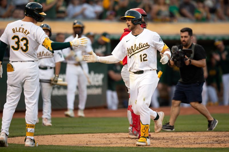 Jul 3, 2024; Oakland, California, USA; Oakland Athletics shortstop Max Schuemann (12) gets a congratulatory handshake from teammate JJ Bleday (33) after hitting a solo home run against the Los Angeles Angels during the fifth inning at Oakland-Alameda County Coliseum. Mandatory Credit: D. Ross Cameron-USA TODAY Sports